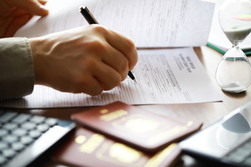 A person filling out travel or immigration paperwork with passports on the desk.